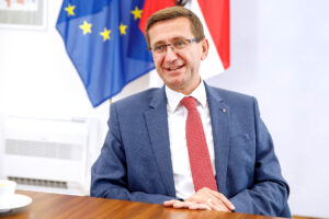 LR Achleitner im Interview mit Österreich Flagge im Hintergrund